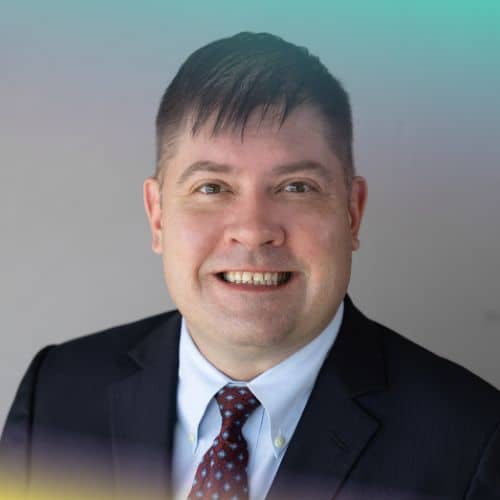 Smiling man in a dark suit and tie, portrait-style business headshot.